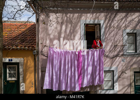 Eine Frau hängt Wäsche auf ihrem Balkon in Lissabon, Portugal. Stockfoto