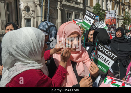 Eine Frau legt letzte Hand an eine palästinensische Flagge sie auf die Wange einer anderen Frau zu Beginn der Al Quds Tag März in London gemalt hat. Stockfoto