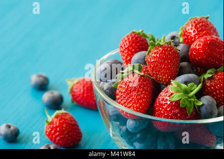 Glasschale mit Sortiment Beeren Heidelbeeren, Erdbeeren über Holz- Tabelle. Tageslicht. Ansicht von oben Stockfoto