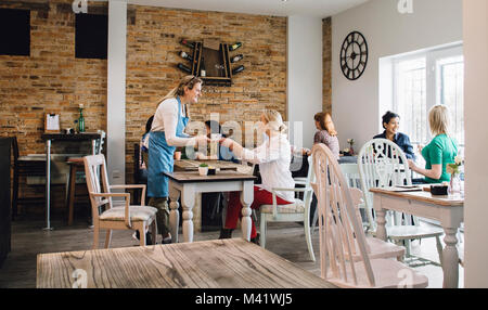 Kellnerin serviert eine Tasse Kaffee mit einem Kunden an einem Tisch in einem Cafe sitzen. Stockfoto