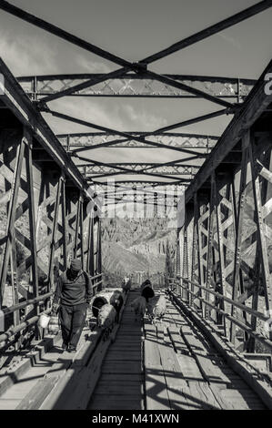 Ein schwarz-weiß Foto eines Hirten zu seiner Herde von Schafen über eine Stahlbrücke mit Holzbohlen Stockfoto