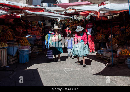 Indigene Frauen tragen traditionelle Hüte und Kleidung zu Fuß durch einen Markt mit ihren Kindern in Sucre, Bolivien Stockfoto