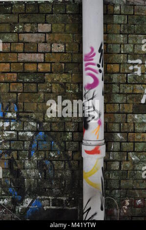 Ein Graffiti - überdachte abflußrohr an einem verschlissenen Mauer in einem Lager befestigt Stockfoto