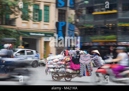 Frau drücken Warenkorb der Kleidung durch die belebten Straßen von Hanoi, Vietnam Stockfoto