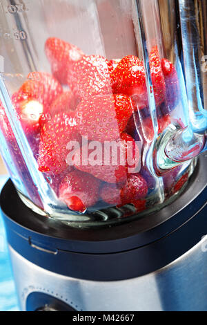 Geschälte reife Erdbeeren in einen Mixer auf einem blauen Holztisch Stockfoto