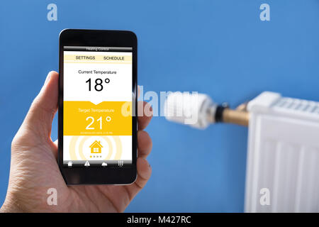 Nahaufnahme der Person Festlegen der Hand Temperatur Thermostat mit Handy zu Hause Stockfoto