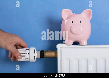 Nahaufnahme der Hand einstellen Thermostat mit Sparschwein am Kühler Stockfoto