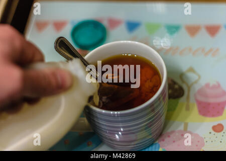 Milch wird in einen Becher Kaffee hinzugefügt. Stockfoto