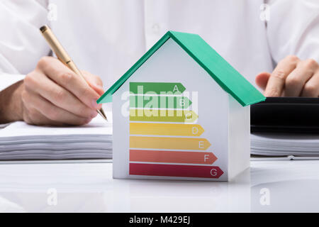 Mittelteil der Geschäftsmann Berechnung Rechnung mit energieeffizienten Diagramm auf Haus Modell im Büro Stockfoto