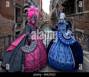 Zwei Frauen in rosa und blau Kostüme und Malte gefiederten Masken Karneval in Venedig verzierten. Frauen stehen auf einer Brücke mit Canal im Hintergrund Stockfoto