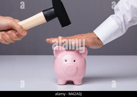 Nahaufnahme der Geschäftsmann Hand sparen Sparschwein aus Hämmern Stockfoto