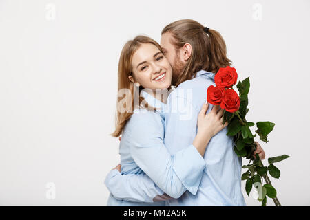 Porträt von einem attraktiven jungen Mann verstecken Blumen von seiner Freundin, bevor er ihr eine Überraschung über Weiß isoliert Hintergrund. Stockfoto