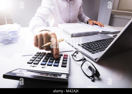 Mittelteil der Geschäftsmann Berechnung der Steuer mit Taschenrechner mit Laptop auf dem Schreibtisch im Büro Stockfoto