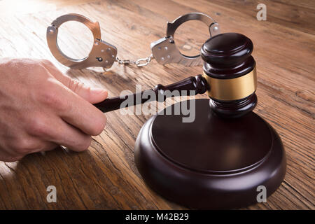Nahaufnahme eines Richters Hand markante Hammer mit Handschellen auf hölzernen Schreibtisch im Gerichtssaal Stockfoto