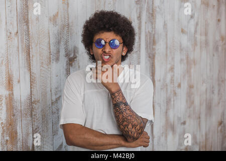 Original sein! Positive lockig behaarten Mann, mit Brille mit kosmischen Muster, während sich gegen alte hölzerne Wand Stockfoto