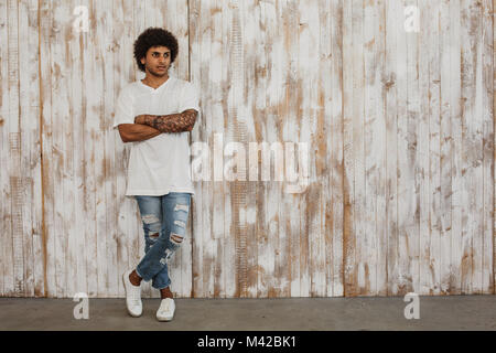 Schöne junge dunkelhäutige Mann mit lockigem Haar steht, gegen retro Holzwand. Moderne Jugend style Kleidung. Stockfoto