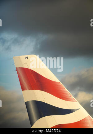 Nahaufnahme der sonnenbeschienenen Schwanzflosse eines British Airways Airbus A319 gegen einen dunklen bewölkter Himmel Stockfoto