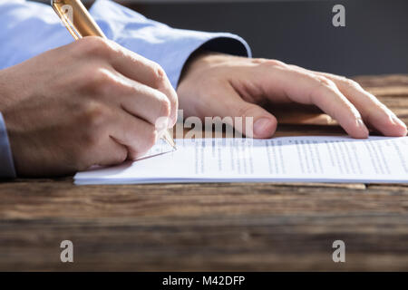 Nahaufnahme der Kaufmann Hand Unterzeichnung Dokument auf hölzernen Schreibtisch Stockfoto