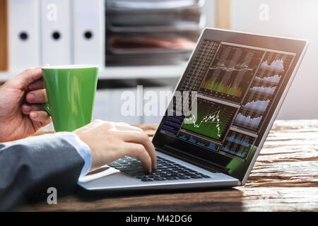 Nahaufnahme eines Stock Market Research wird das Arbeiten mit Diagrammen auf den Laptop über Holz- Schreibtisch Stockfoto