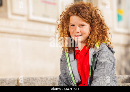 Portrait von lächelnden Teenager lockigen Haaren Junge sitzt draußen und Suchen an Kamera Stockfoto