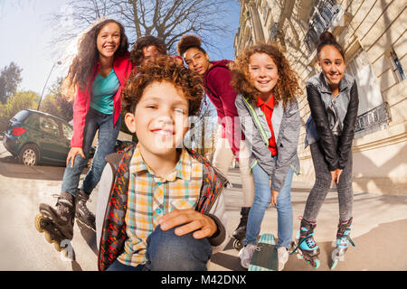 Multiethnischen Teenager Jungs und Mädchen mit Inline-skates oder skateboards Spaß an Straßen in der Stadt Stockfoto