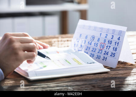 Der Unternehmer Hand Prüfungsschema im Kalender mit dem Kalender auf hölzernen Schreibtisch Stockfoto