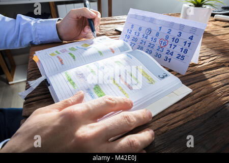 Der Unternehmer Hand Prüfungsschema im Kalender mit dem Kalender auf hölzernen Schreibtisch Stockfoto