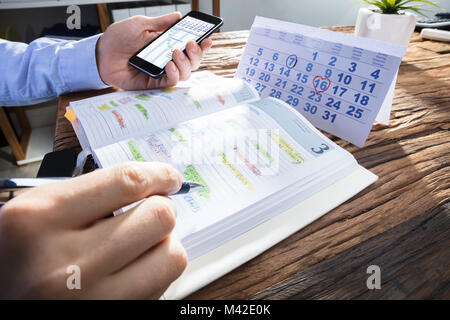 Der Unternehmer Hand Smartphone mit Gantt-diagramm auf Bildschirm während der Planung im Tagebuch Stockfoto