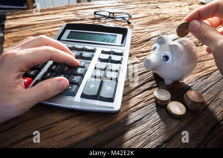 Person's Hand einfügen Münze in Piggy Bank während der Verwendung von Taschenrechner Stockfoto