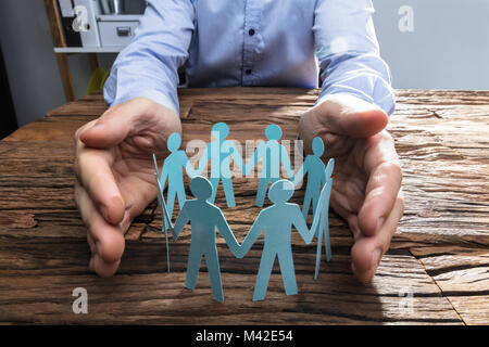 Nahaufnahme einer einer Person schützende Hand Papier schneiden Sie Abbildung auf hölzernen Schreibtisch Stockfoto