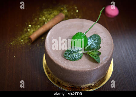 Chocolate Cheesecake mit grün Kirsche und minzeblatt auf Woodden Hintergrund. Süßigkeiten Wüste Stockfoto