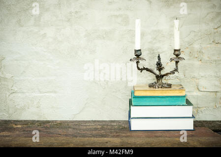 Bunte Zusammensetzung mit Vintage alte Bücher, Tagebuch auf Holzterrasse Tabelle und beige konkreten Hintergrund. Bücher stapeln mit klassischen Leuchter an der Spitze. Stockfoto