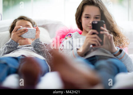 Schwestern mit Smartphones im Schlafzimmer Stockfoto