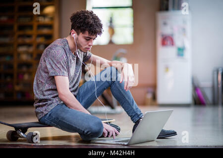 Jungen Erwachsenen männlichen sitzen auf mit Laptop skateboard Stockfoto
