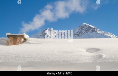 Die rauchenden Kamin von einem Dach Schnee im Winter in den Schweizer Bergen. Stockfoto