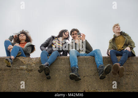Gruppe junger Freunde sitzen auf einer Mauer bei einem Smartphone suchen Stockfoto