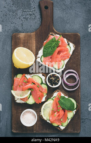 Toast Brötchen mit Lachs, Gurke und Frischkäse auf altem Schneidebrett. Table Top Aussicht, getönten Bild Stockfoto