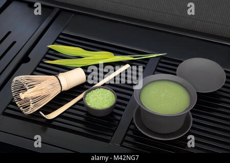 Grüner japanischer Matcha Tee mit Pulver und Gesundheit Getränk in Schale mit Schneebesen und stick Magnetrührer mit Bambus Blatt auf schwarz Fach. Stockfoto