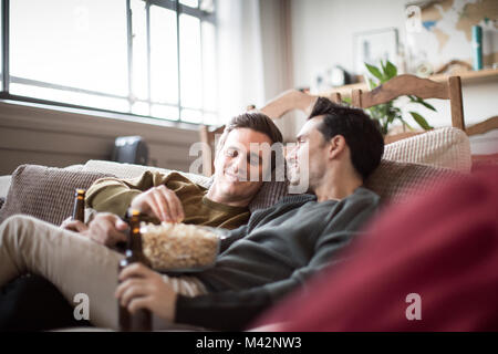 Junge männliche Paar entspannt auf einem Sofa mit Bier und Popcorn Stockfoto