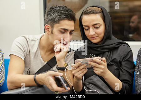 Teheran, Iran - 28. April 2017: Eine junge Iranische Paar verwendet mobile Geräte, während sie sich in einer U-Bahn Auto unterwegs sind. Stockfoto