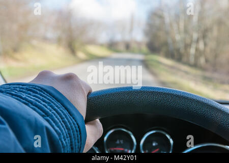 Hand am Lenkrad, Blick aus dem Auto. Im Freien gibt es Straßen, Bäume und blauer Himmel. Stockfoto