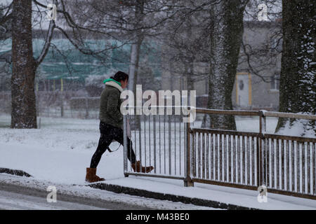 Dundee, Schottland, Großbritannien. 14. Februar, 2018. UK Wetter: Starker Schneefall in Nordostschottland mit Temperaturen nahe dem Gefrierpunkt. Eine Frau eingehüllt vom kalten Winterwetter Überquerung der Schnee Straße in der Nähe von Arldler Dorf in Dundee, UK abgedeckt. Credits: Dundee Photographics/Alamy leben Nachrichten Stockfoto