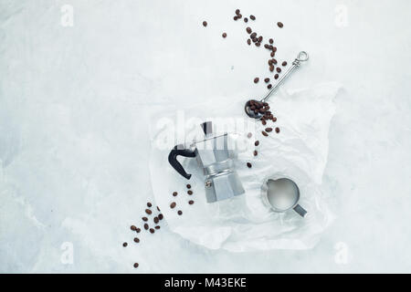 Kaffee Konzept flach auf einem weißen konkreten Hintergrund legen. Minimalistischer Bild mit kopieren. Moka Kanne, Kaffee tastin Löffel, Milchkännchen und Kaffee Stockfoto
