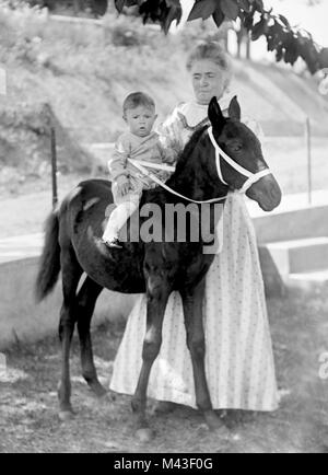 Oma wirft mit Kleinkind Enkel auf ein Pony, Ca. 1910. Stockfoto