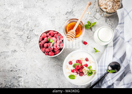 Zutaten für Sommer gesundes Frühstück, Getreide (Hafer), frische Himbeeren, Minze, Joghurt, Honig, an der konkreten Hintergrund, kopieren Raum t Stockfoto