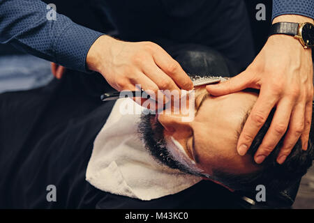 Schließen Sie herauf Bild der Friseur rasieren ein Mann mit einem scharfen Stahl gestochen. Stockfoto