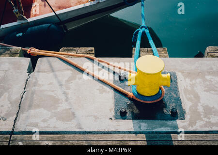 Gelber Ankerplatz auf einem hölzernen Pier mit einem angedockten Boot im Hintergrund Stockfoto