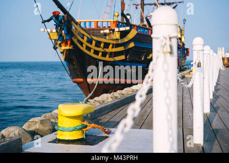 Sopot, Polen. Festmachen Poller auf einem hölzernen Pier mit einem angedockten Piratenschiff im Hintergrund Stockfoto