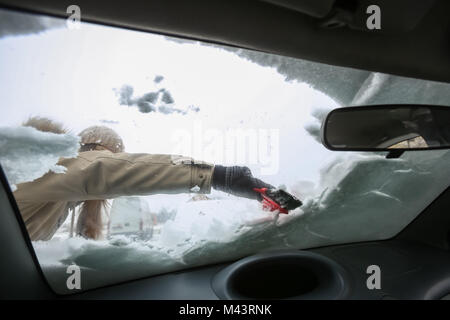 Eine Frau, die Reinigung der Schnee von der Windschutzscheibe gesehen aus dem Inneren des Autos. Stockfoto