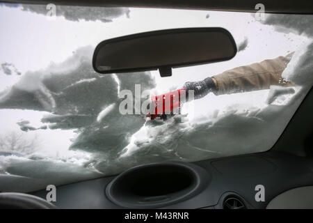 Eine Frau, die Reinigung der Schnee von der Windschutzscheibe gesehen aus dem Inneren des Autos. Stockfoto